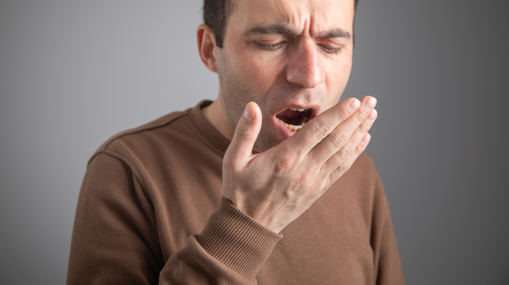 Man checks his breath with his hand. The concept of halitosis